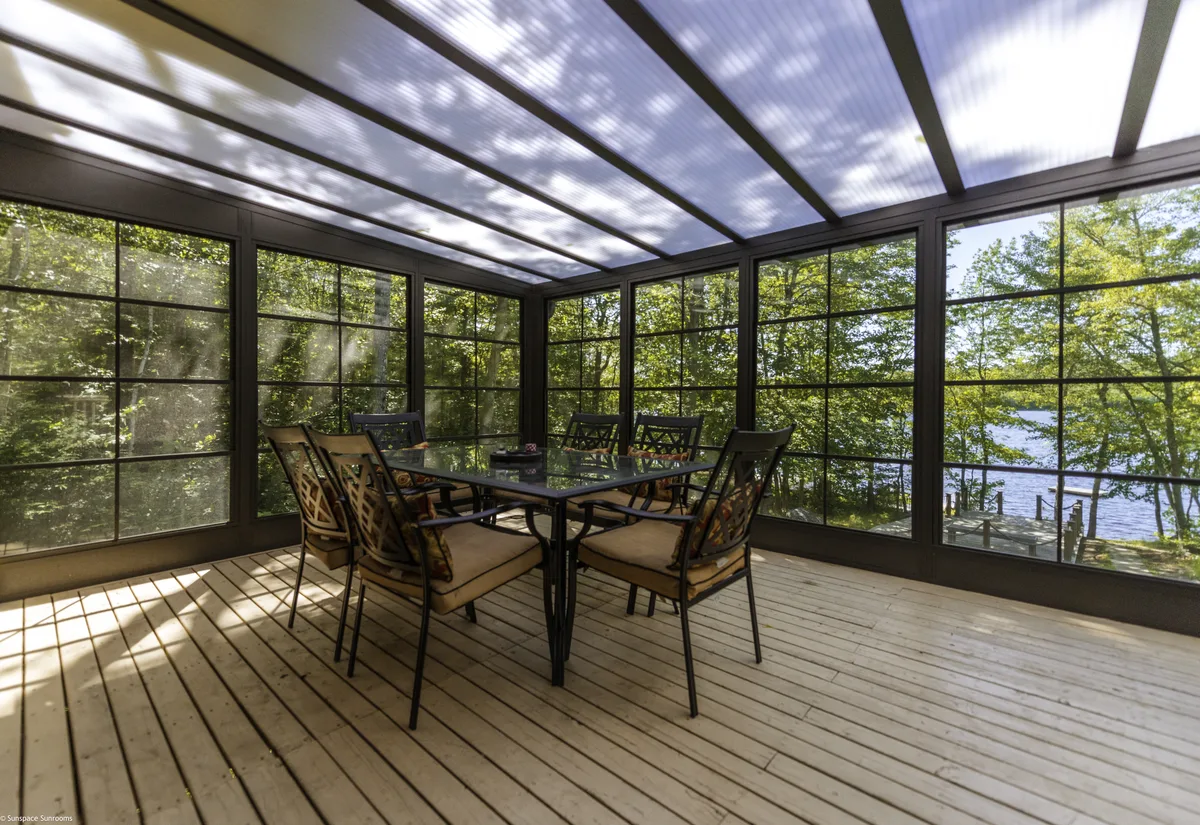 Une véranda avec une table et des chaises, mettant en valeur les toits de patio qui améliorent la lumière naturelle et le confort de l'espace.